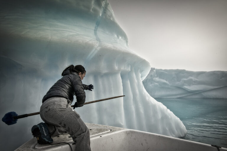Greenland: the dilemma of ice, a man and boat push an iceberg through the water, so that it doesn't drag down their fishing nets 