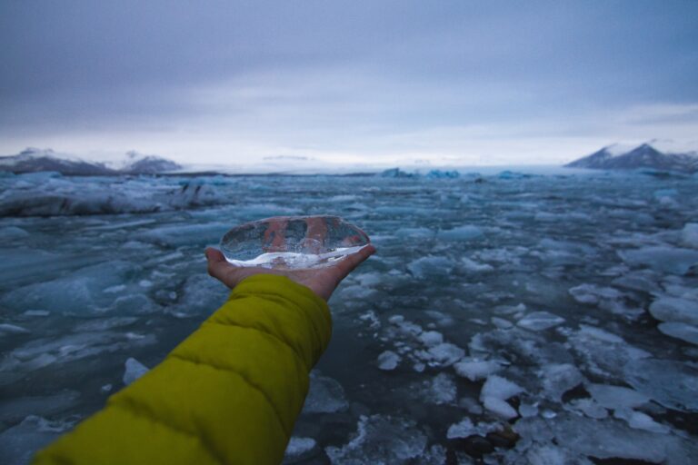 Hand holding ice with a frozen sea under a cloudy sky in Iceland on the background